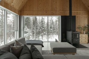L’intérieur d’un chalet accueillant, avec une grande fenêtre, un canapé, un banc et un poêle à bois.