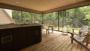 Terraza de madera con hidromasaje, mesa de picnic y sillas Adirondack, con vista a un bosque.