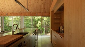 Una cocina moderna con armarios de madera, un lavamanos de acero inoxidable y un ventanal con vistas a un bosque.