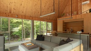 Un interior moderno con un sofá gris, techo de madera, ventanas amplias y una zona de cocina.