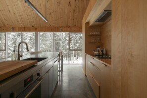 A modern kitchen with a wooden interior, large windows, and a view of snow-covered trees. - Woodland Getaway | Hot Tub • Sauna • Hike • Fire (Chertsey)