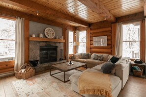 A cozy log cabin interior with a stone fireplace, wooden ceiling, and a comfortable seating area.