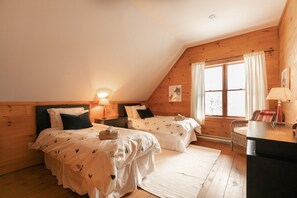 A cozy bedroom with two beds, a desk, and a window with curtains.