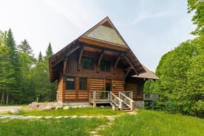 Eine Blockhütte mit einem steilen Satteldach, einer Holzterrasse und einem Steinfundament.