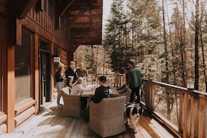 Eine Holterrasse mit Korbmöbeln, einem Hund und einem Wald im Hintergrund.
