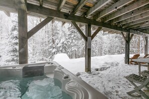 A wooden outdoor hot tub area with snow-covered trees in the background.