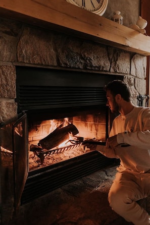 A fireplace with logs burning, a stone wall, and a clock above it.