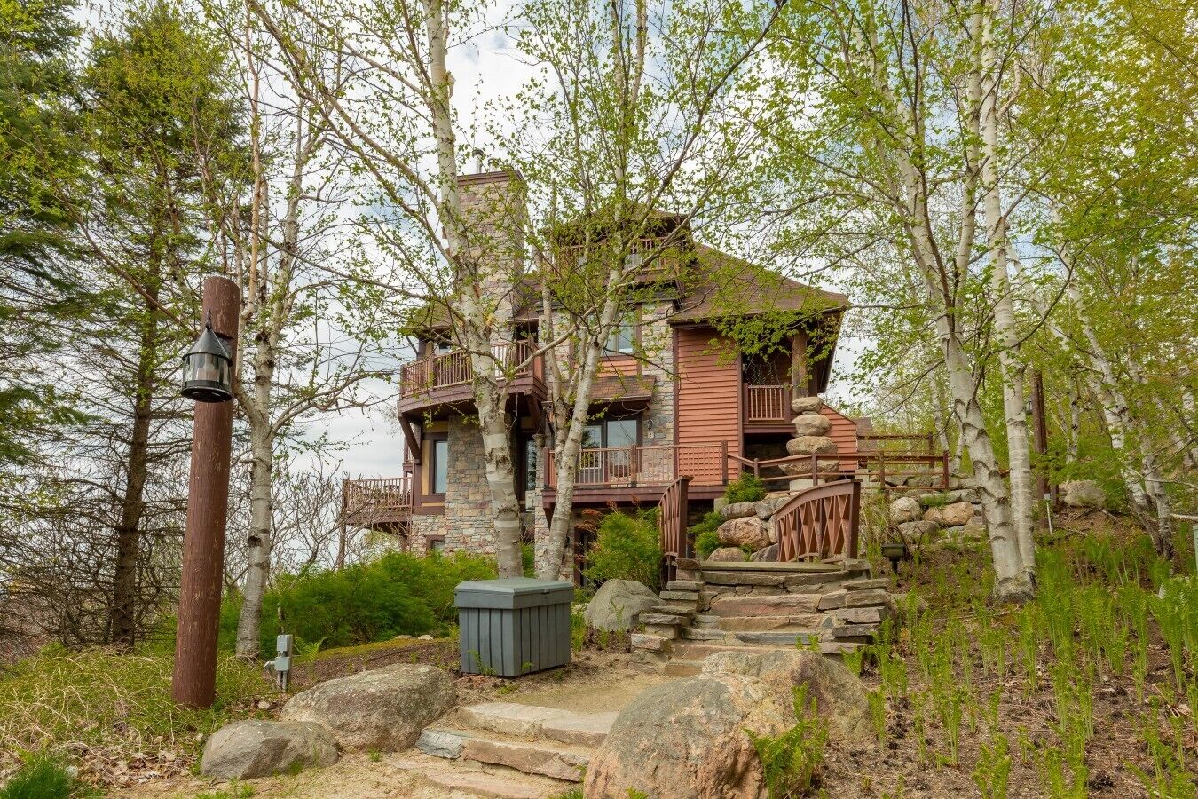 A rustic cabin with a stone foundation, wooden balconies, and a stone staircase leading to the entrance.