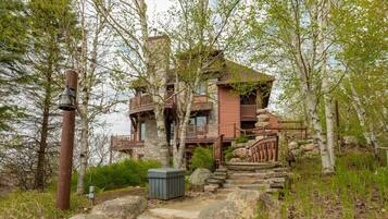 A rustic cabin with a stone foundation, wooden balconies, and a stone staircase leading to the entrance.