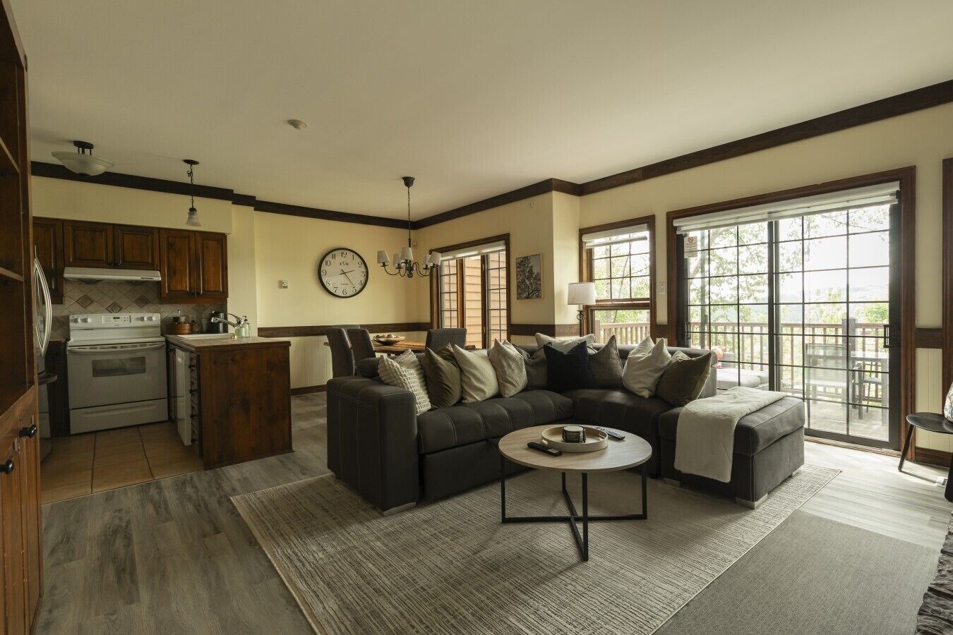 A living room with a sectional sofa, a dining area, a kitchen with modern appliances, and large windows offering a view.
