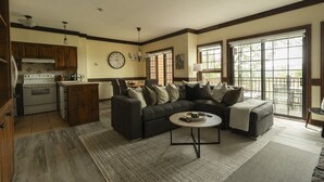 Una sala de estar con un sofá modular, un comedor, una cocina con electrodomésticos modernos y ventanas amplias que ofrecen una vista.
