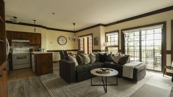 A living room with a sectional sofa, a dining area, a kitchen with modern appliances, and large windows offering a view.