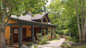 A rustic cabin with a porch, surrounded by trees and a gravel path. - Just steps from Tremblant • Free shuttle (Mont-Tremblant)