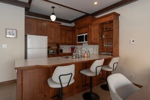 A kitchen with wooden cabinets, a white refrigerator, a microwave, a sink, and a bar area with stools. - Just steps from Tremblant • Free shuttle (Mont-Tremblant)