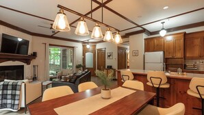 A dining area with a wooden table, chairs, and pendant lights. There is a kitchen with wooden cabinets and a refrigerator. - Just steps from Tremblant • Free shuttle (Mont-Tremblant)