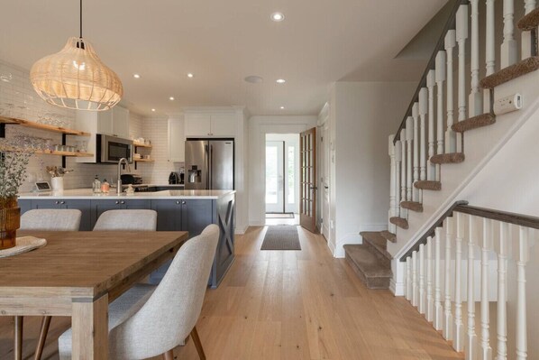 Une cuisine moderne avec des meubles blancs, un îlot central et un coin repas comprenant une table et des chaises en bois.