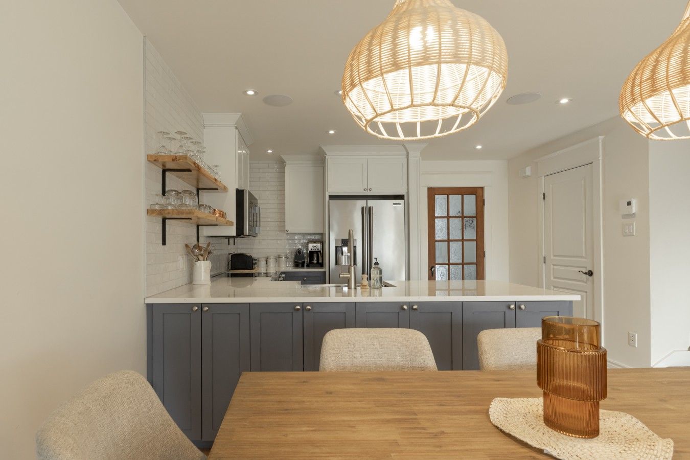 A modern kitchen with a central island, grey cabinets, and a wooden dining table.