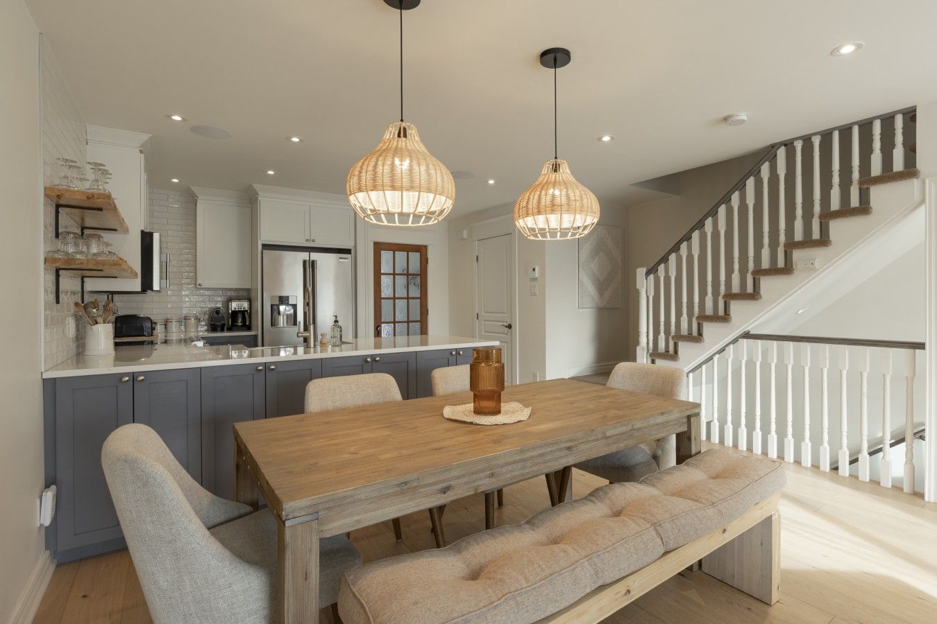 A modern kitchen with a central island, grey cabinets, and a wooden dining table with benches.
