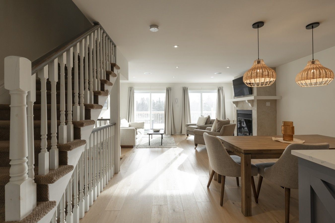 A spacious living area with a staircase, a dining table with chairs, and a fireplace.