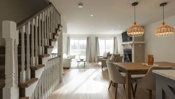 A spacious living area with a staircase, a dining table with chairs, and a fireplace.