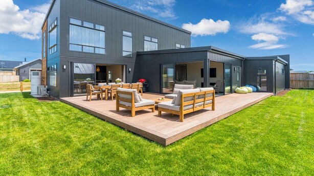 Une maison moderne à deux étages dotée d’un patio aménagé avec du mobilier d’extérieur.