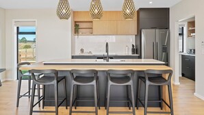 Une cuisine moderne dotée d’un îlot central, de tabourets de bar, de luminaires suspendus et offrant une vue sur l’extérieur.