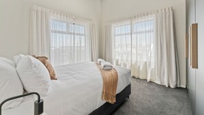 Une chambre d’hôtel avec un grand lit, deux fenêtres avec des rideaux légers, un ventilateur de plafond et une vue sur l’extérieur.