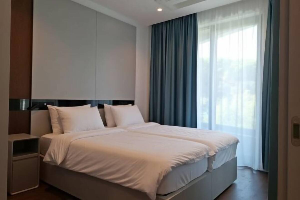 Ein modernes Hotelzimmer mit einem großen Bett, einem Nachttisch und Blick ins Freie durch transparente Vorhänge.