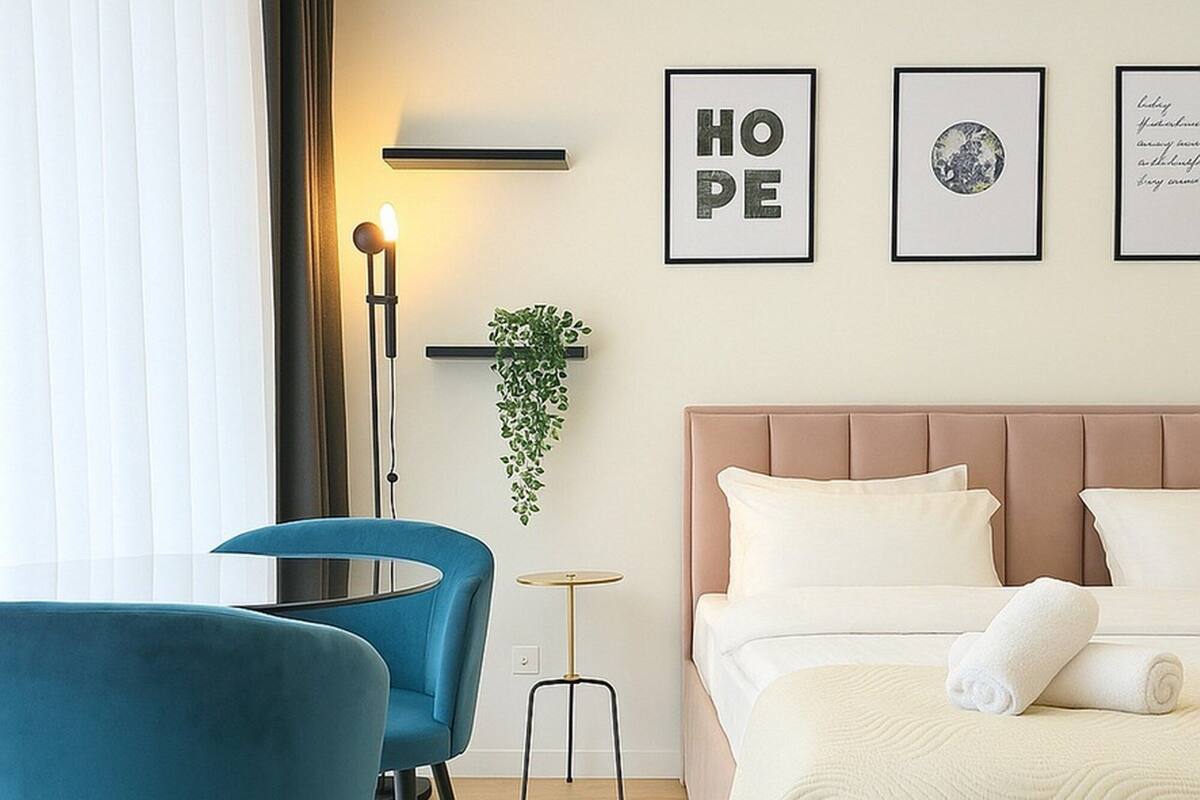 Ein Hotelzimmer mit einem Bett, einem Schreibtisch mit Stuhl, einer Stehlampe und gerahmten Bildern an der Wand.