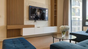 A modern living room with a flat-screen TV mounted on the wall, a glass coffee table, and two blue sofas. - Waterfront Collection Apartments (Belgrade)