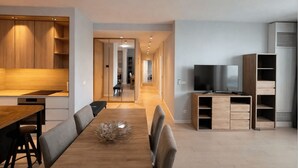 A modern living room with a wooden dining table, a TV, and built-in shelving. - Waterfront Collection Apartments (Belgrade)