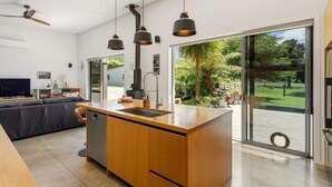 Una cocina moderna con una isla central, un comedor con sofá y un amplio ventanal corredera que da a un jardín.