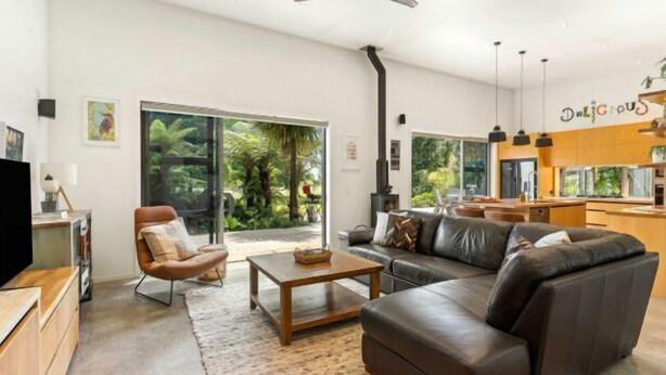 Una sala de estar moderna con sofá, sillón y mesa de centro. Se aprecia un amplio ventanal con vistas a la vegetación.
