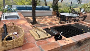 Zona cuina exterior amb taulell de maó, eines de barbacoa i un rentapeus.