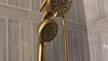 A gold-colored showerhead with a flexible hose, mounted on a wall with a textured tile pattern.