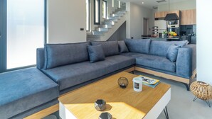 Uma sala de estar moderna com um sofá seccional cinza, uma mesa de centro de madeira e uma escada que dá para uma área de cozinha.