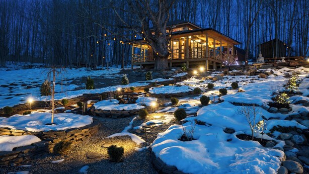 A lodge with a large tree in the foreground, a stone pathway, and snow-covered ground.