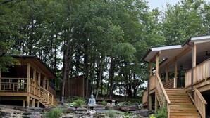A wooden cabin with a porch and a stone pathway leading to a meditation area with statues.