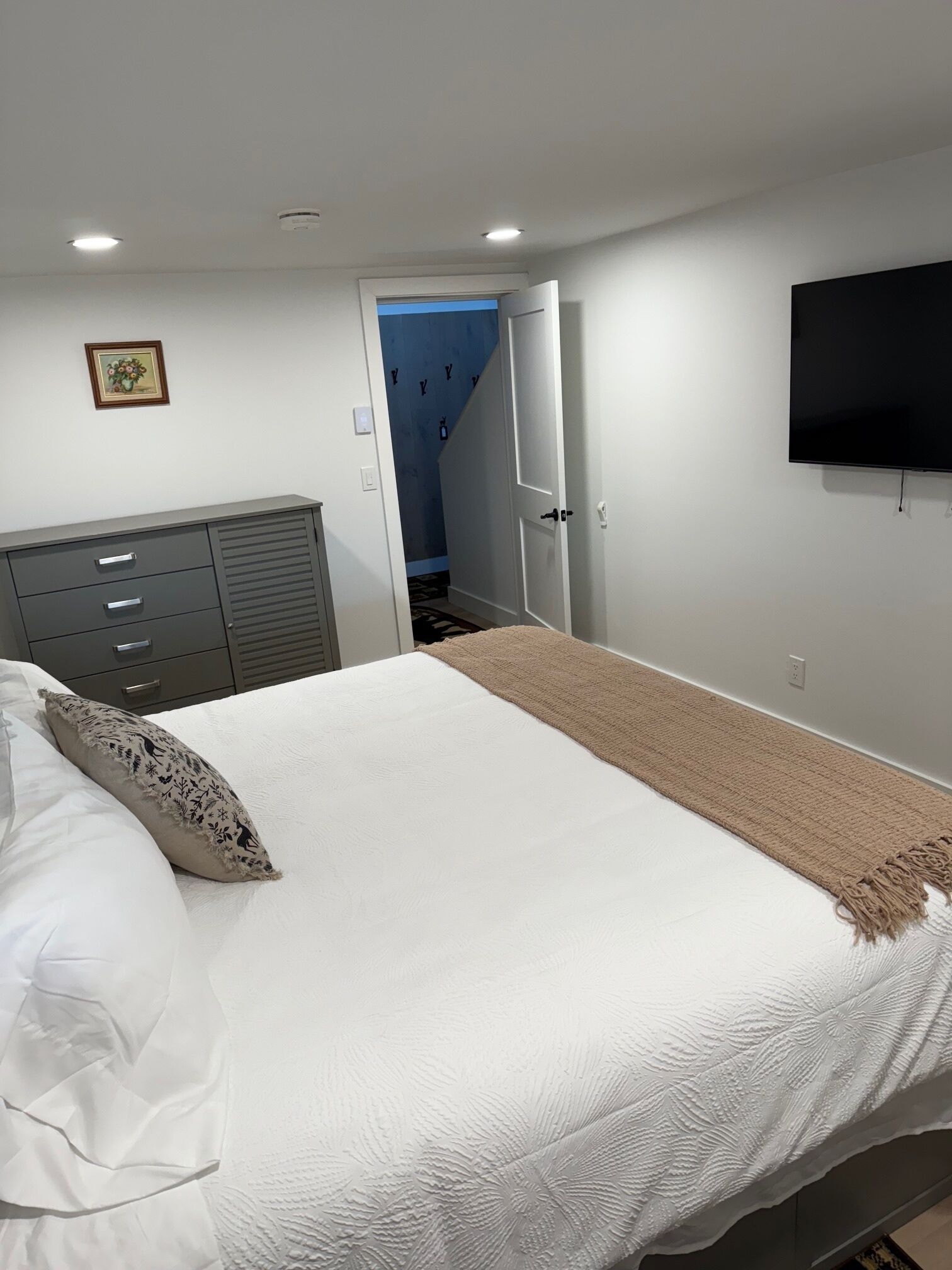 Een slaapkamer met een bed, een dressoir, een televisie en een deur naar een gang.