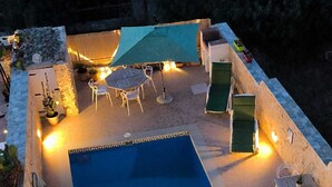A rooftop swimming pool with a blue water feature, surrounded by a stone wall, and equipped with outdoor seating and lighting. - il figolla (Xaghra)