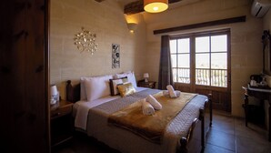 A bedroom with a large bed, wooden beams, a window with a view, and a wall-mounted air conditioner. - il figolla (Xaghra)