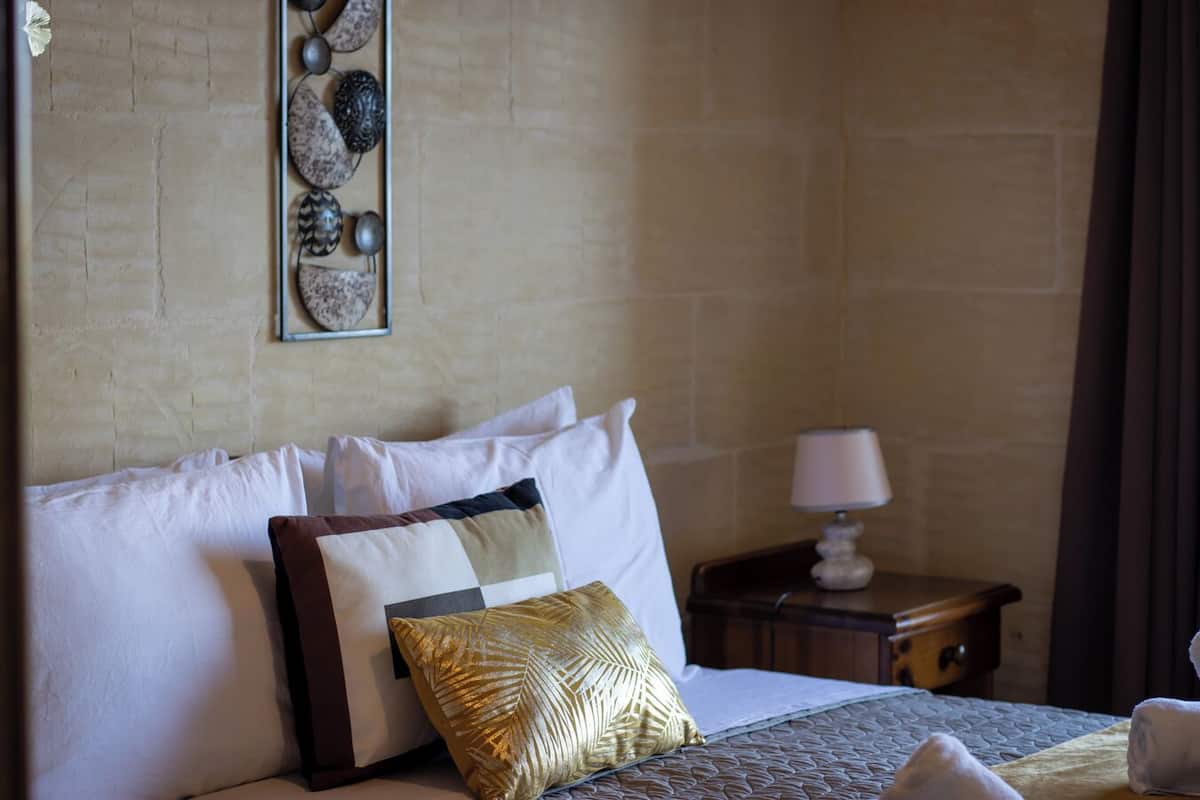 Habitación de hotel con cama, almohadas, mesita de noche y lámpara.