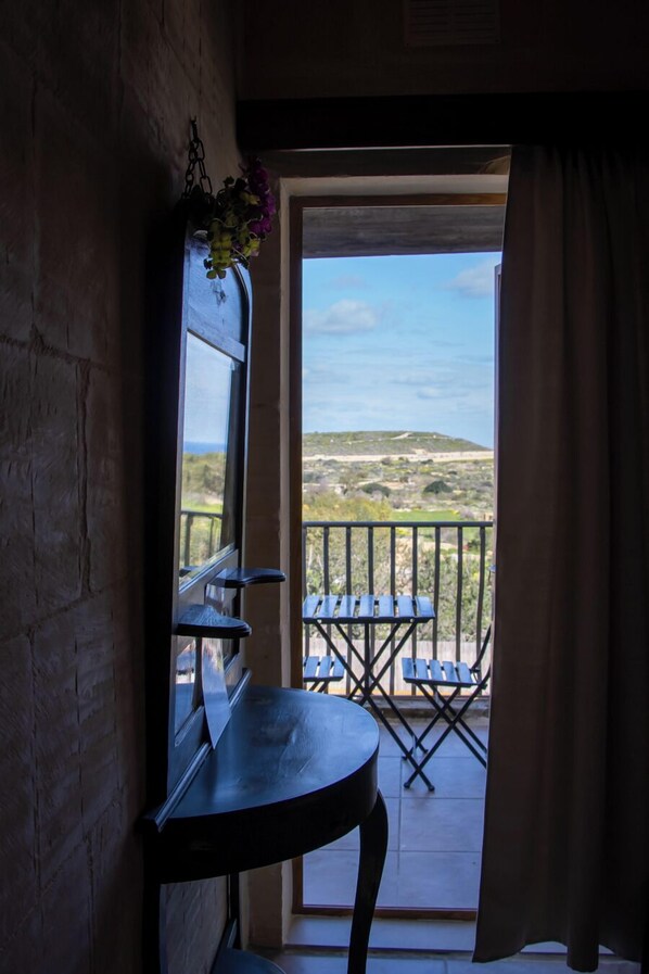 A balcony with a table and chairs, a hanging flower arrangement, and a view of the landscape. - il figolla (Xaghra)