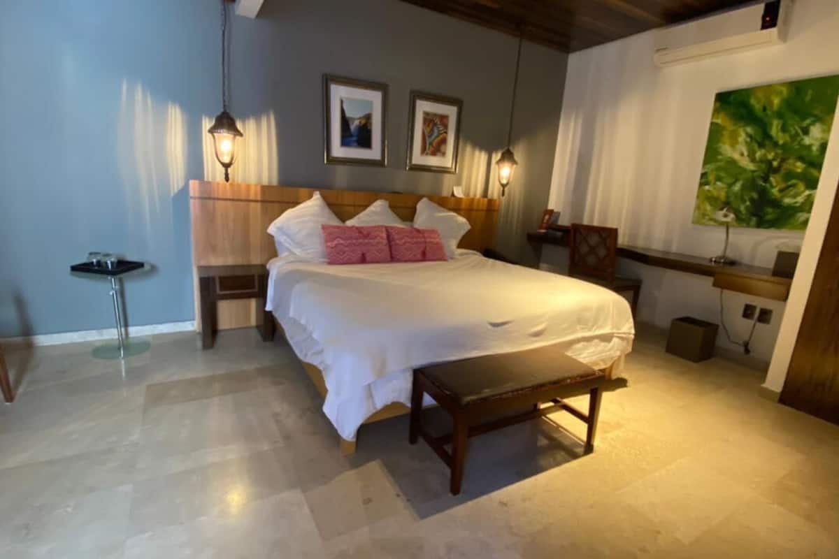 Un dormitorio con cama, mesitas de noche, un banco y obras de arte en las paredes.