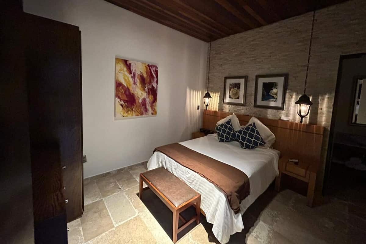 Un dormitorio con cama, banca, decoración en la pared y dos lámparas fijadas a la pared.