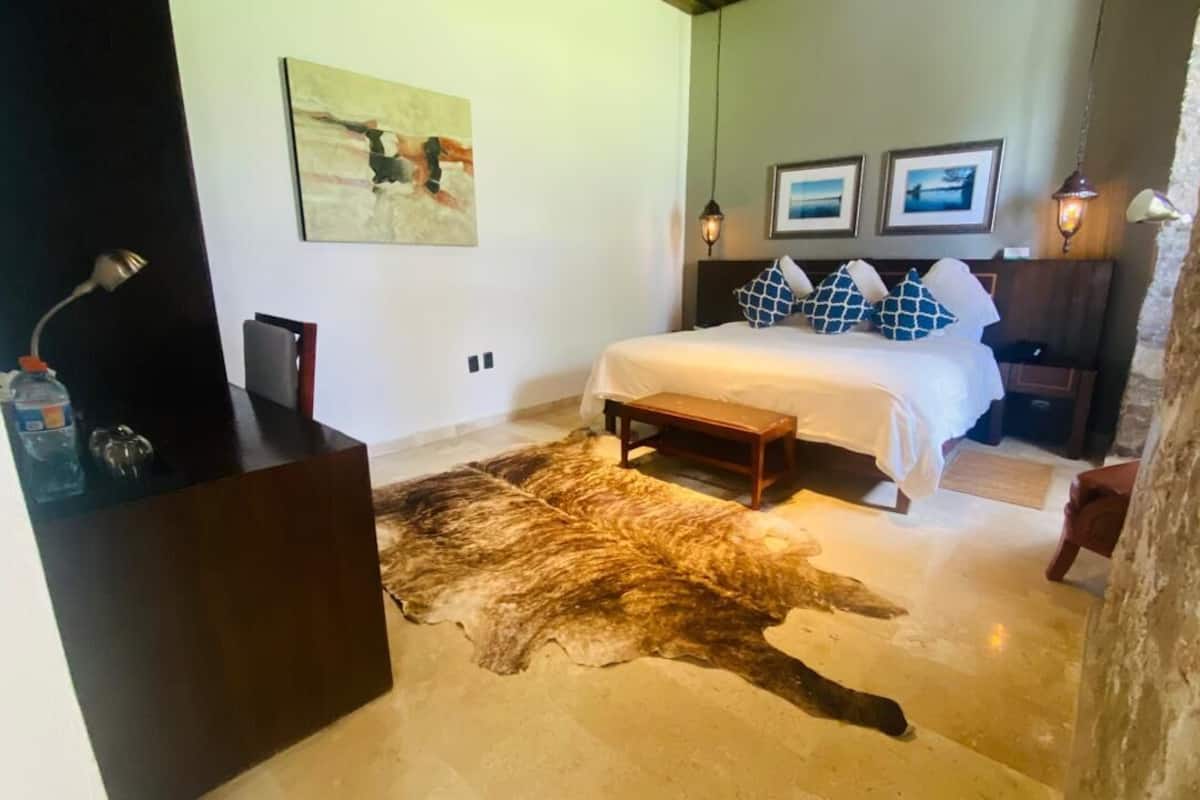 Un dormitorio con un tapete de piel grande, una cama con almohadones estampados, una mesita de noche y una lámpara fijada a la pared.