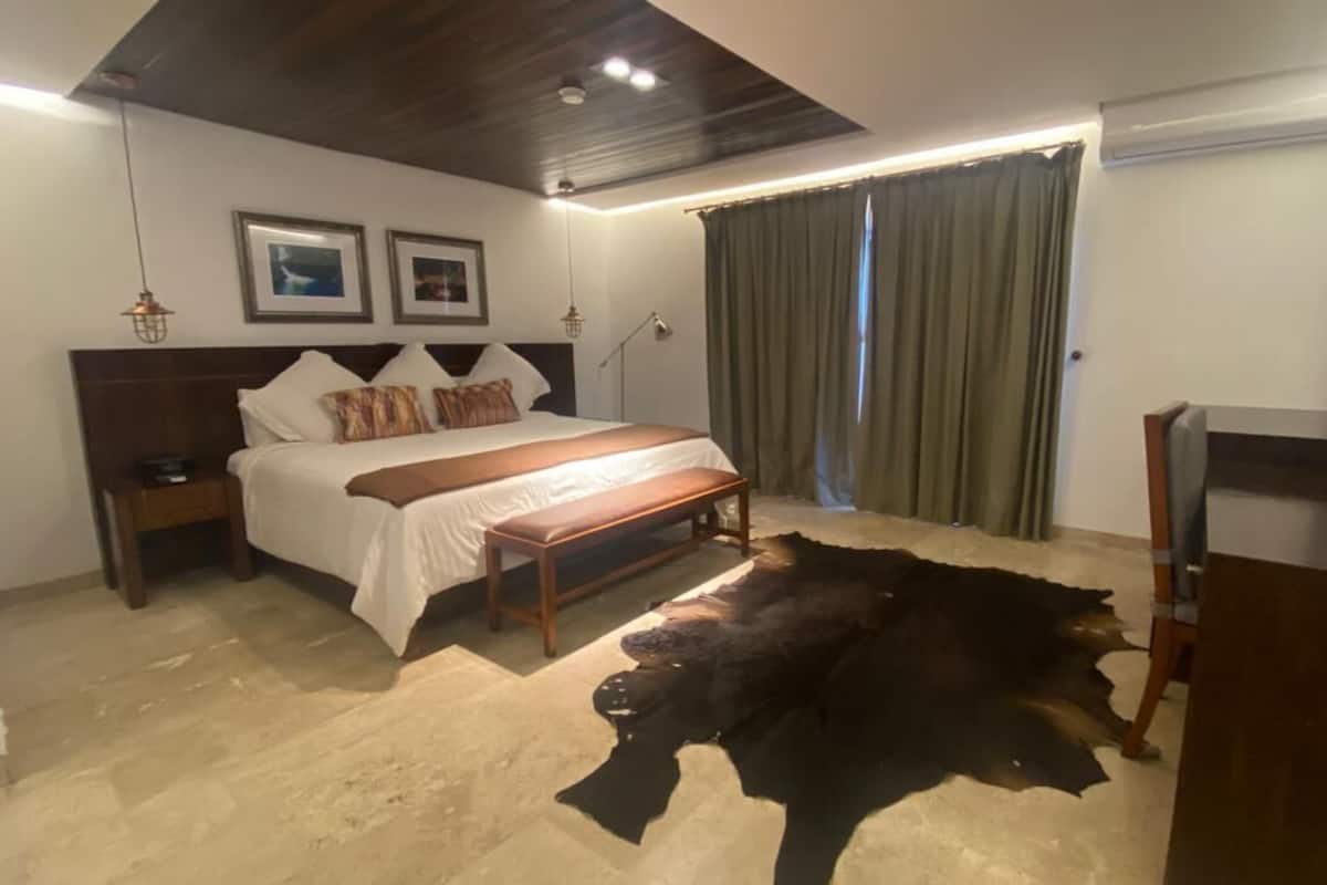 Un dormitorio con cama, mesitas de noche, un banco, una alfombra de piel grande y un escritorio con silla.
