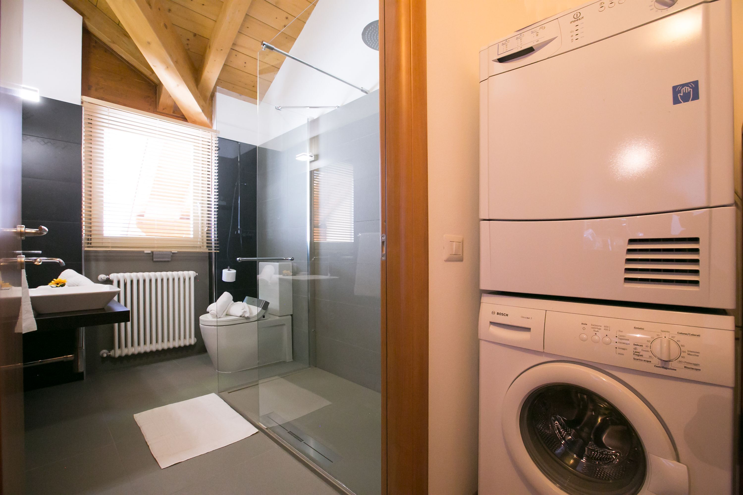A modern bathroom with a glass shower enclosure, a built-in sink, and a stacked washer and dryer unit.