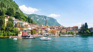 Un pittoresco borgo costiero con edifici colorati, una torre campanaria e barche sull'acqua.