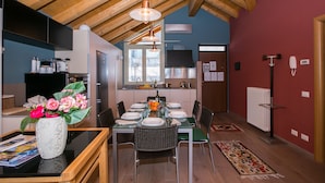 Una cucina moderna con travi in legno, una zona pranzo con tavolo apparecchiato per quattro e un soggiorno con una parete rossa e un termosifone.